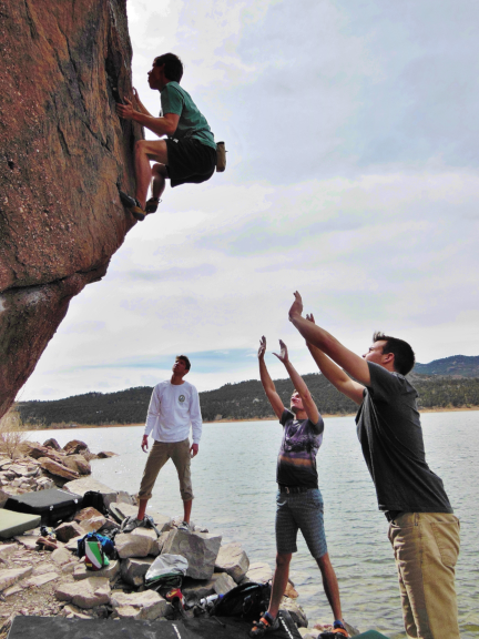 a rock climber with spotters below ready to catch him if he falls. People helping people.